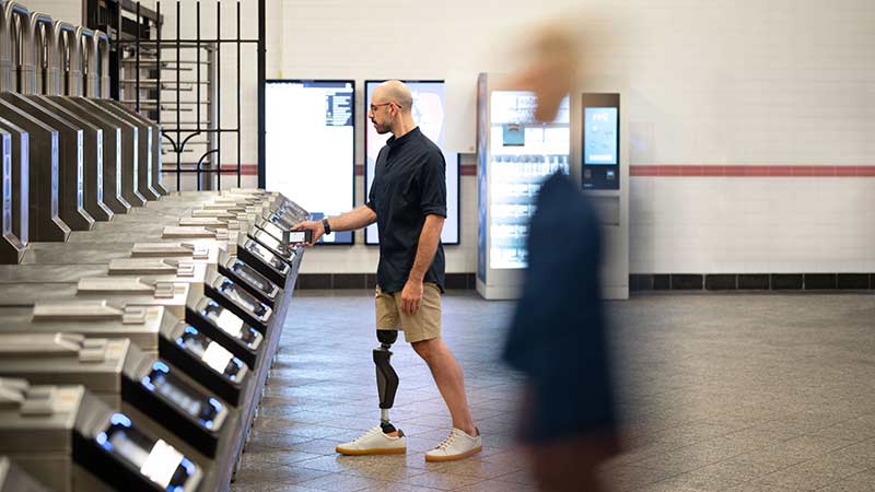 Man with a prosthetic leg taps his payment-enabled device to enter a subway station