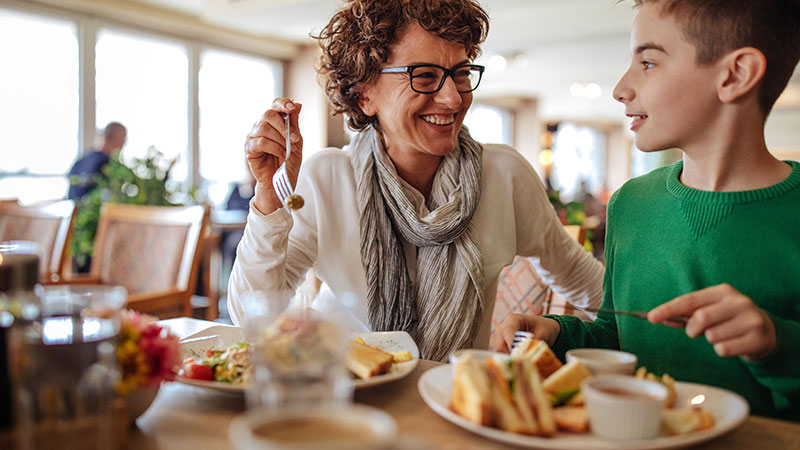 A woman and boy smiling and enjoying their food at a restaurant.