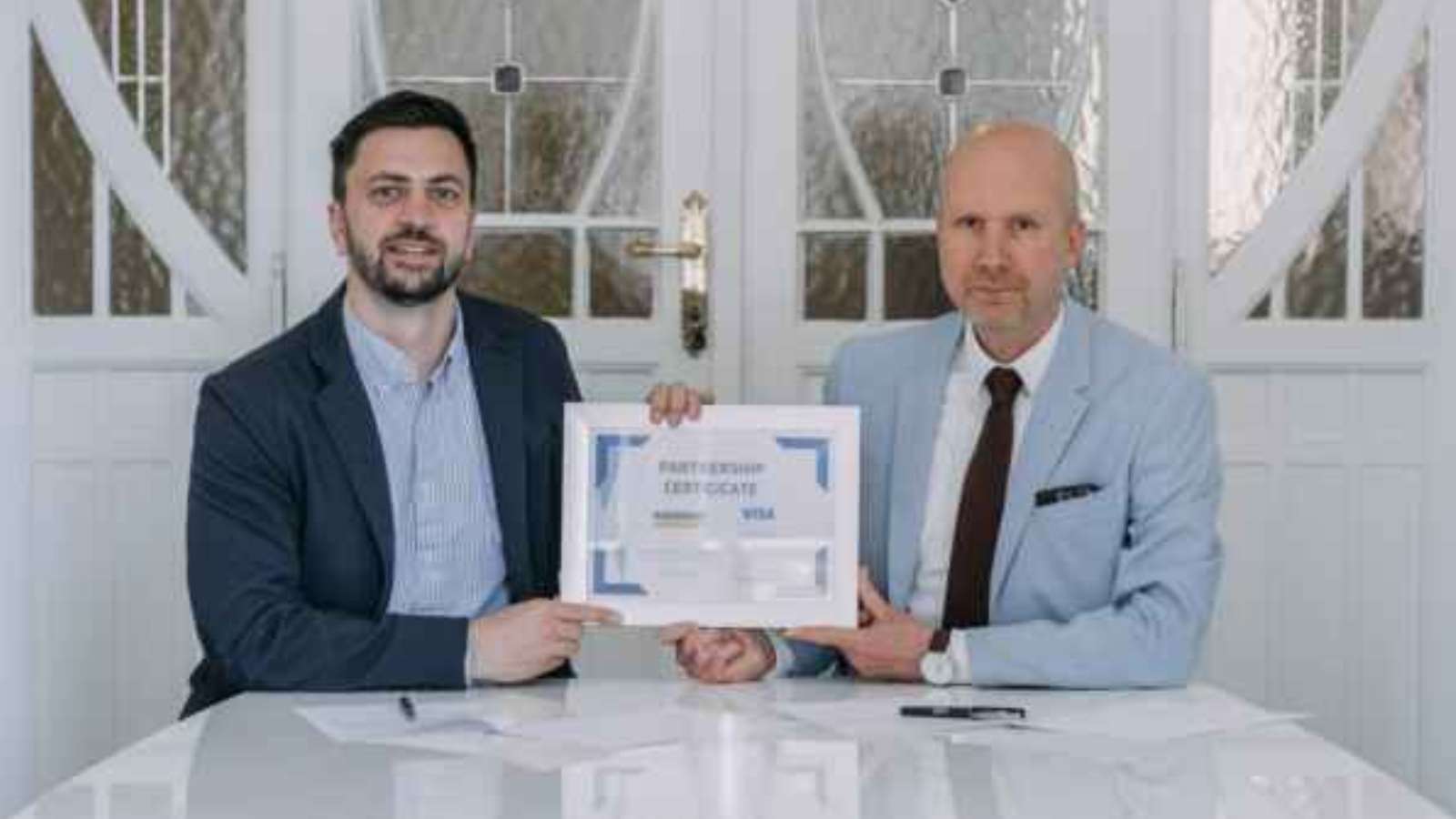 Two men hold a certificate of partnership between VISA and Moris Design