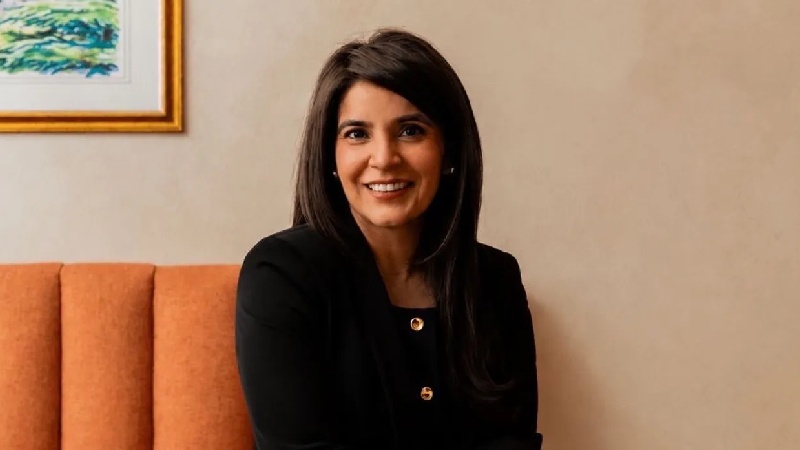 Smiling woman in black attire seated on an orange sofa indoors