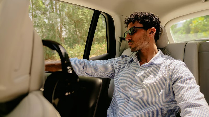Man wearing sunglasses and a striped shirt sitting in the back seat of a car