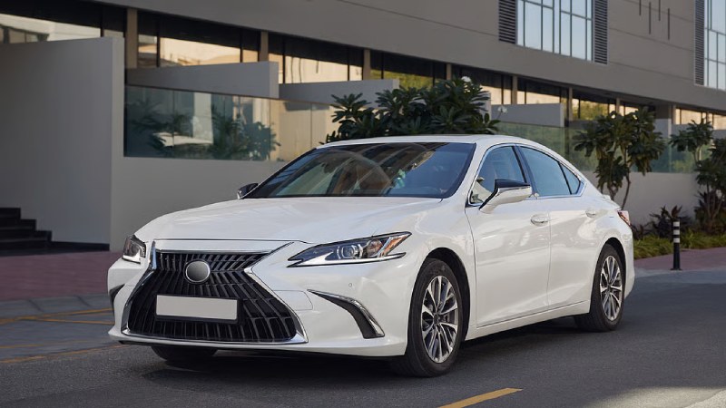 White luxury sedan parked on a city street in front of a modern building